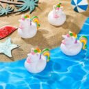 cztery Gumowe zabawki do kąpieli - kaczka/jednorożec położone na piasku obok basenu z wodą