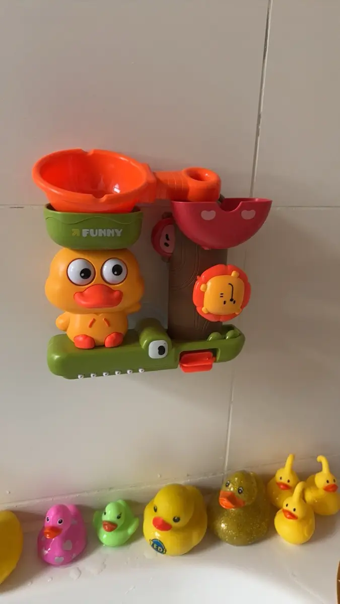zabawka do kąpieli z kaczką przyczepiona do kafelek nad wanną, pod nią kilka gumowych kaczek