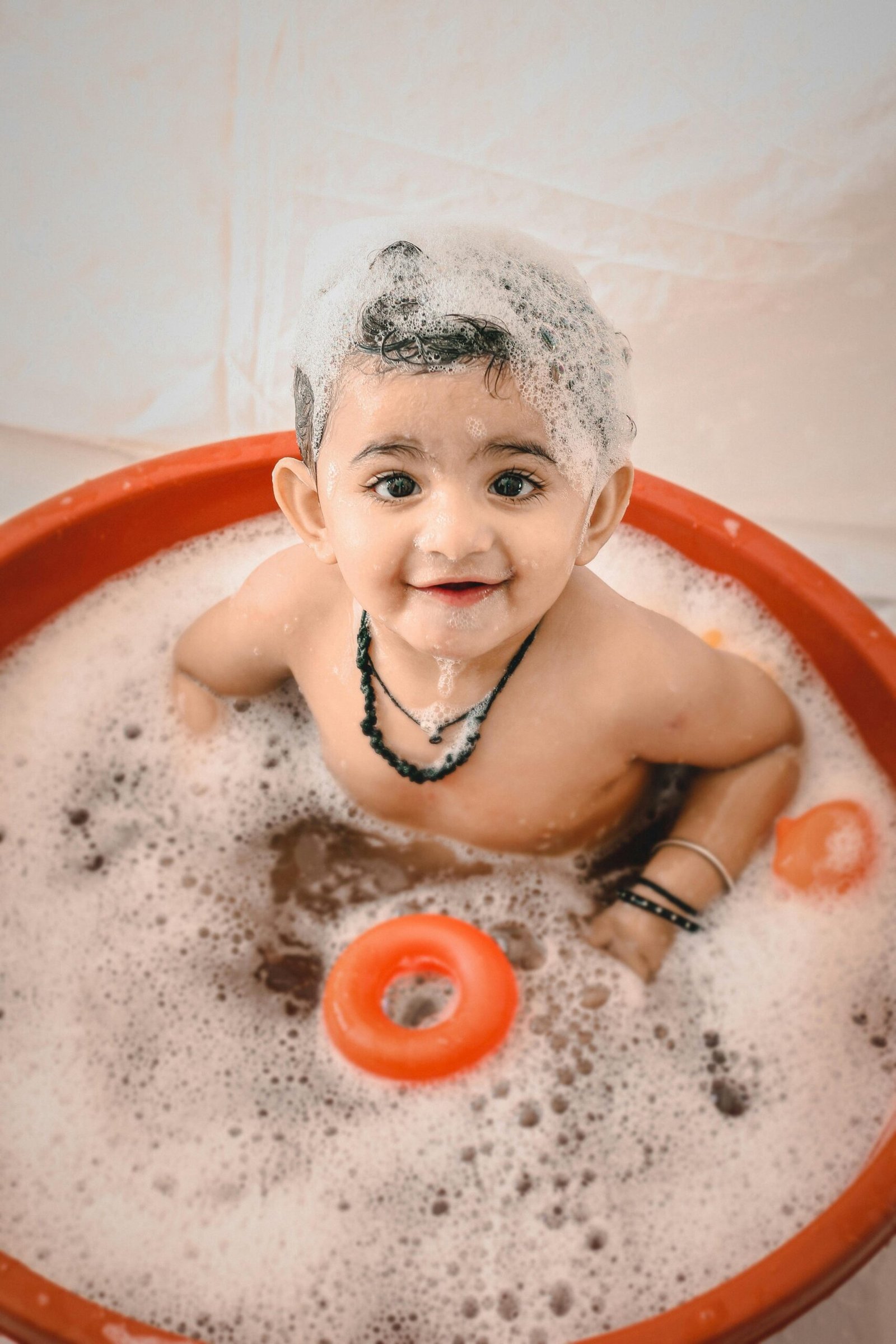 chłopiec uśmiechający się w wannie, obok niego pomarańczowe zabawki do kąpieli