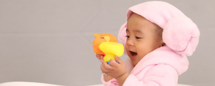 niemowlak w rózowym ręczniku bawiący się gumowymi zabawkami do kąpieli dla niemowlaka